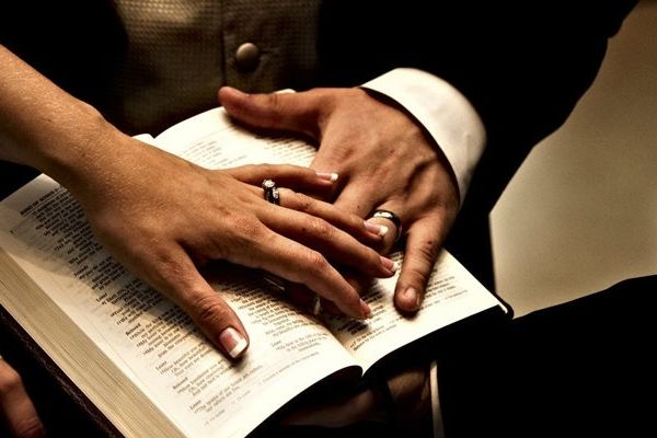 husband and wife with hands on opened bible